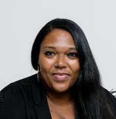 Portrait of a professional Black woman with long black hair, wearing a black blazer, smiling at the camera.